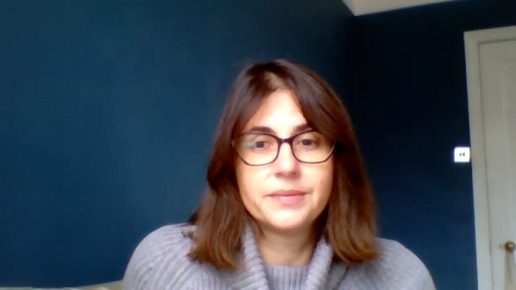 Foto der Autorin mit Brille und grauem Pullover vor einer dunkelblauen Wand